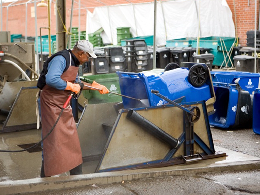 A photo of a man washing out an Ocean Core recycling cart